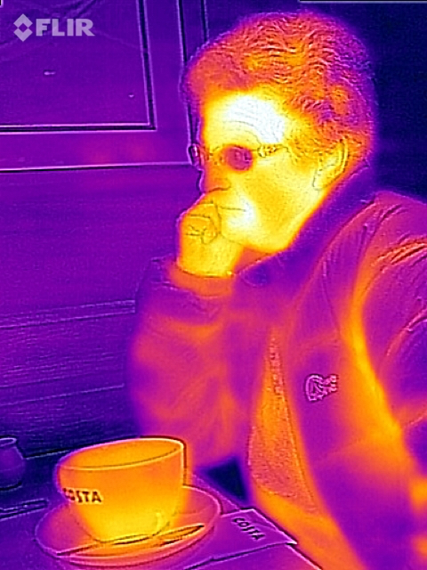 My wife, sat drinking coffee, and wearing a quilted jacket.